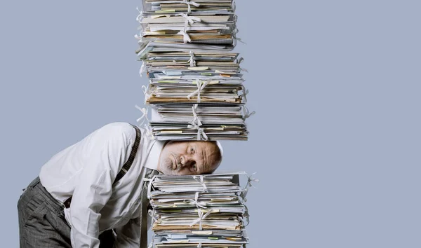 Stressed businessman under a pile of paperwork, he is overwhelmed by work