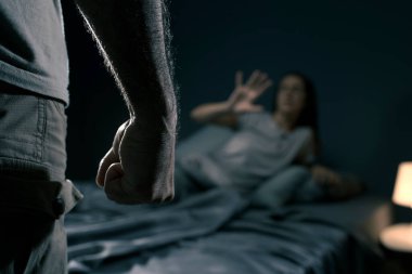 Bir adam yatak odasında bir kadını tehdit ediyor, kadın korkmuş ve yatakta yatıyor, aile içi şiddet kavramı.