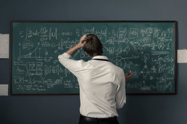 Genç matematikçi problemleri çözüyor ve yazı tahtasına formüller yazıyor.