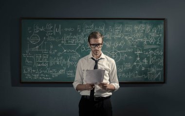 Tahtanın önünde duran ve formülleri, matematiği ve akademik araştırma kavramını açıklayan kendinden emin genç matematik profesörü.