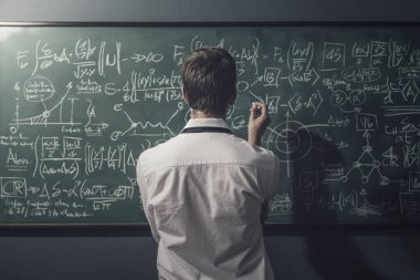 Genç matematikçi problemleri çözüyor ve yazı tahtasına formüller yazıyor.