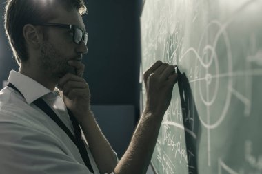 Genç zeki matematikçi tahtaya matematik formülleri çiziyor ve düşünüyor: problemleri çözüyor ve yeni teoriler keşfediyor