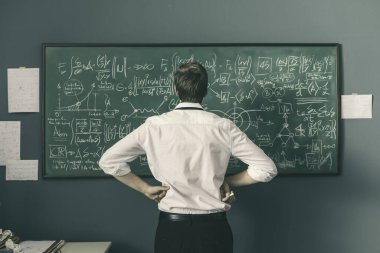 Genç matematikçi problemleri çözüyor ve yazı tahtasına formüller yazıyor.