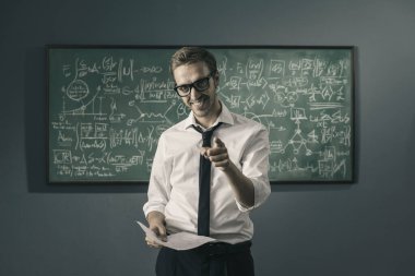 Kendine güveni tam bir profesör elinde matematik formülleriyle tahtada duruyor ve kamerayı işaret ediyor.