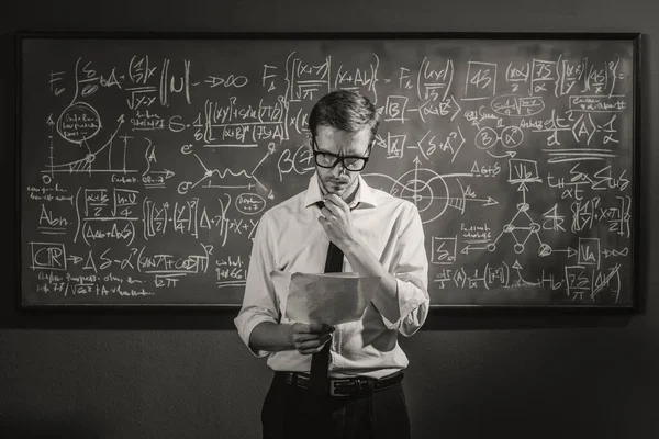 Confident young math professor standing in front of the chalkboard and explaining formulas, mathematics and academic research concept