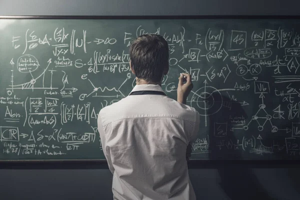 若い数学者は問題を解決し 黒板に数式を書く バックビュー — ストック写真