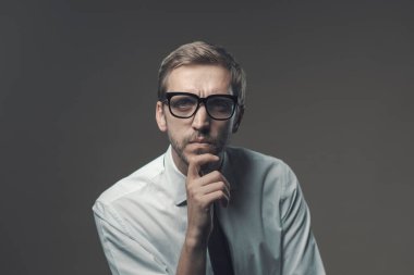 Eli çenesinde dalgın bir adam, şüpheli bir ifadeyle kameraya bakıyor.