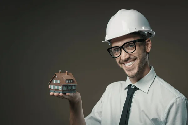 Smiling architect holding a model house, real estate and construction industry concept