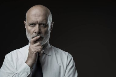 Çenesi, iş stratejileri ve liderlik konseptiyle düşünen kendinden emin orta yaşlı bir işadamının portresi.