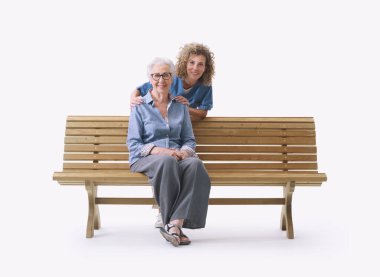 Bankta oturan ve omuzlarını tutan mutlu yaşlı bayan, beyaz arka planda izole edilmiş yaşlı bakım konsepti.