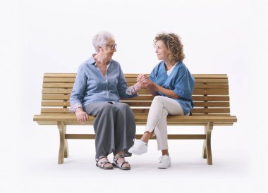 Dost canlısı hemşire yaşlı bir bayanla bankta oturuyor ve onu rahatlatıyor, elini tutuyor, beyaz arka planda tek başına.