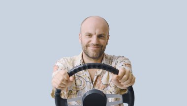 Elinde direksiyon tutan ve görünmez bir araba kullanan gülümseyen bir adam kameraya bakıyor, izole edilmiş.