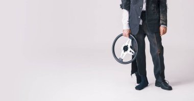 Yırtık takım elbiseli bir adamın komik bir stüdyo portresi. Elinde direksiyon simidi olan komik bir kazayı, beceriksiz bir başarısızlığı ve beyaz arka planda komik bir felaketi temsil ediyor..