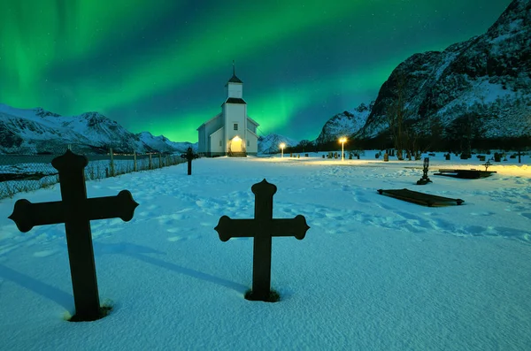 Northern lights over winter landscape with church and graveyard