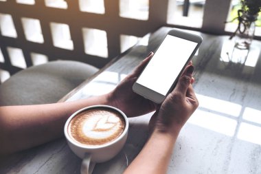 Kadının görüntüsünü mockup holding beyaz cep telefonu ile boş okul sırası perde ve kahve fincanı kafede masada eller