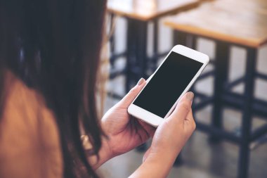 Kafede boş siyah masaüstü ekranı olan beyaz cep telefonu tutan bir kadının görüntüsü