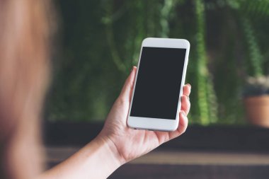 Bir kadın tutarak ve beyaz bir akıllı telefon ile boş siyah okul sırası perde ile bakarak görüntüsünü mockup yeşil doğa arka plan bulanıklık