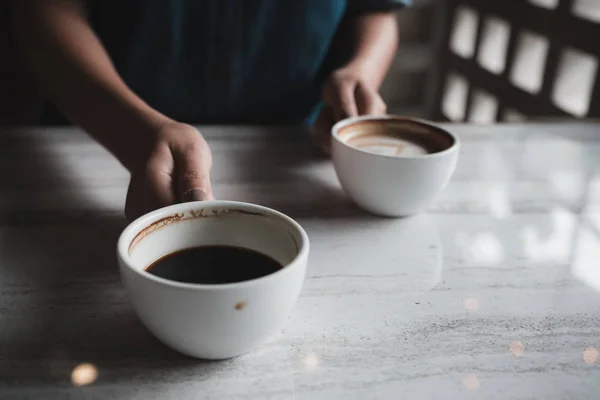 カフェのテーブルでホット コーヒーの つの白いカップを保持している手のクローズ アップ画像 — ストック写真