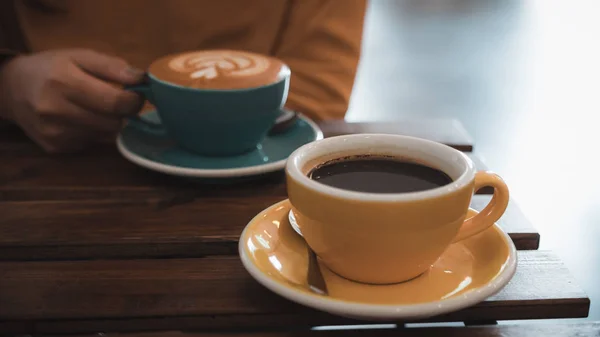 カフェでホット コーヒーの青いコップとテーブルに別の黄色いカップを保持している女性のクローズ アップ画像 — ストック写真