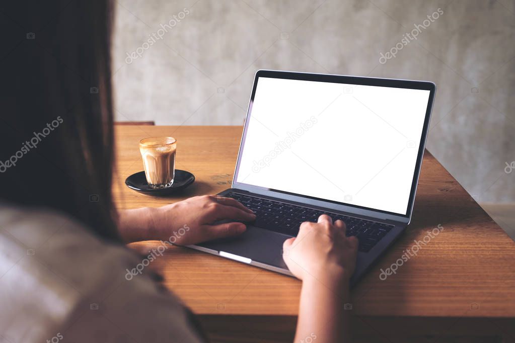 Mockup image of a woman using laptop with blank white desktop screen with coffee cup on wooden table 