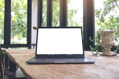 Boş beyaz masaüstü ekranı olan dizüstü bilgisayarın doğa arka planına sahip eski ahşap masa üzerindeki görüntüsü