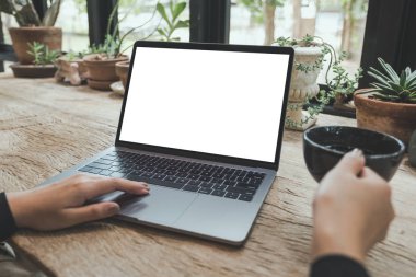 Mockup görüntü kullanarak ve vintage ahşap masa kafede kahve yudumlarken boş beyaz masaüstü ekran ile Laptop yazarak kadının