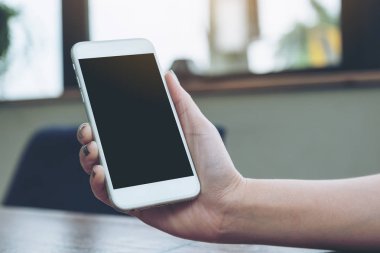 Ahşap masanın üzerine boş siyah perde ile beyaz cep telefonu tutan bir kadın görüntüsünü mockup