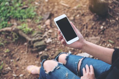 Mockup görüntü boş masaüstü ekran beyaz cep telefonuyla yerdeki açık otururken tutan kadın