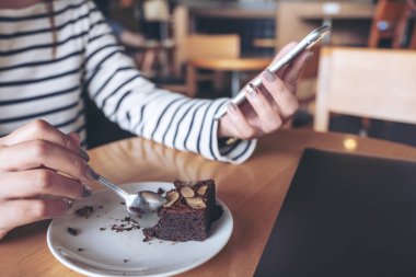 Portre resim kullanarak ve seyir akıllı telefon Cafe brownie Pasta yerken bir kadın
