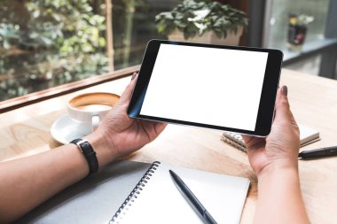 Siyah tabletli, beyaz ekranlı, defter ve kahve fincanı olan bir kadının el resmi. 