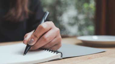 Tahta masaya beyaz boş bir defter yazan bir kadının yakın plan resmi. 
