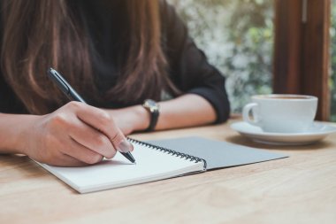 Bir kadının el resmi, beyaz boş bir deftere yazılmış, kahve fincanı da ahşap masaya. 