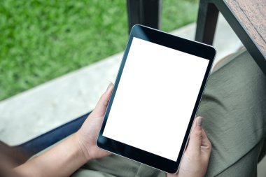 Yeşil Doğa geçmişi olan kafede otururken yukarıdan mockup kadının görüntüsünü holding siyah tablet pc ile beyaz boş ekran eller