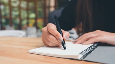 Tahta masaya beyaz boş bir defter yazan bir kadının yakın plan resmi. 