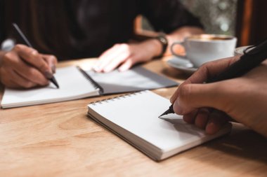 Üstünde beyaz bir boş defter ile kahve fincanı ofiste ahşap tabloda yazmak iki iş adamı closeup görüntü