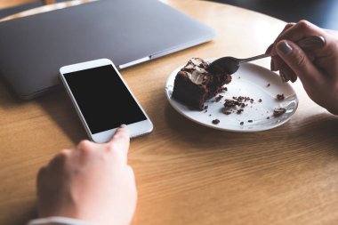 Mockup görüntü beyaz cep telefonu ile boş siyah okul sırası perde gösteren bir kadının zevk kafede brownie kek yeme