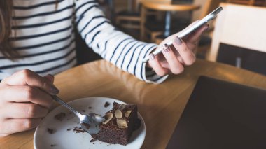 Portre resim kullanarak ve seyir akıllı telefon Cafe brownie Pasta yerken bir kadın