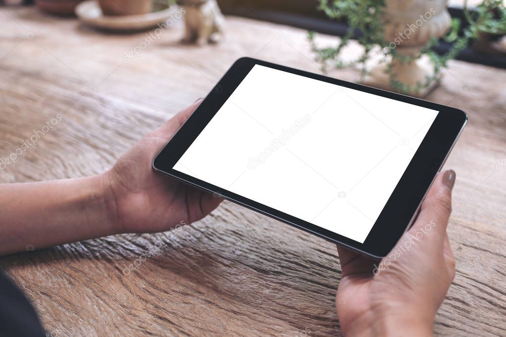 Mockup image of hands holding black tablet pc with blank white screen on vintage wooden table 