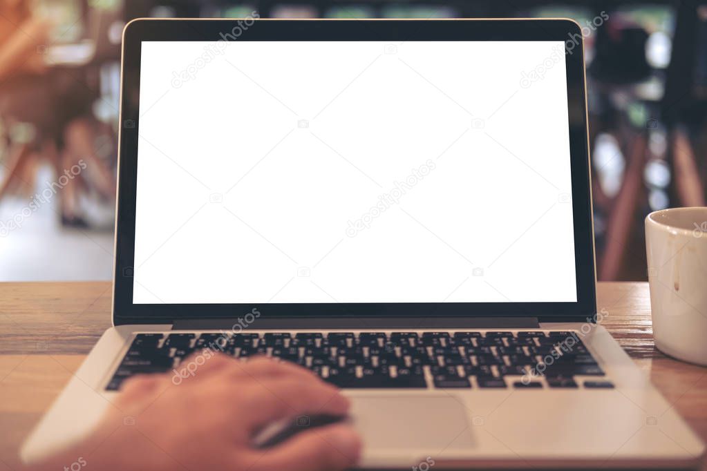 Mockup image of a hand using laptop with blank white desktop screen with coffee cup on wooden table in cafe