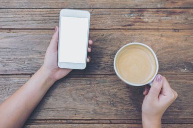 Mockup görüntü boş beyaz ekran ve sıcak kahve Cafe antika ahşap masa üzerinde tutan el ile beyaz cep telefonu