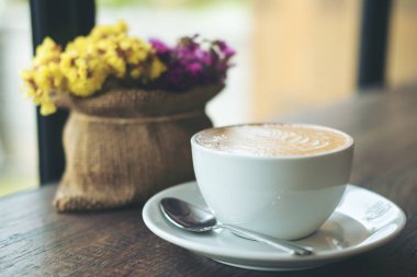 Sıcak latte kahve vintage ahşap masa üzerinde bir Vazoda Çiçekler ile beyaz bir fincan