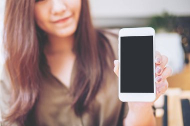 Güzel bir kadın tutarak ve beyaz cep telefonu ile boş siyah perde ile gülen yüz vintage ahşap kafede gösterilen mockup görüntü