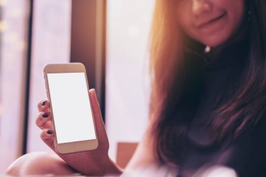 Güzel bir kadın tutarak ve modern kafede beyaz cep telefonu boş beyaz ekran ve gülen yüz ile gösterilen mockup görüntü