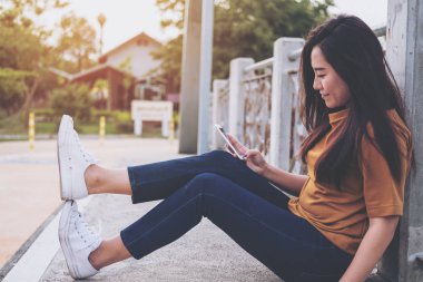 Güzel bir kadın köprüde otururken akıllı telefonu kullanıyor ve ona bakıyor.