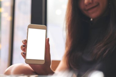 Güzel bir kadın tutarak ve modern kafede beyaz cep telefonu boş beyaz ekran ve gülen yüz ile gösterilen mockup görüntü