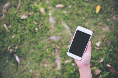 Beyaz cep telefonu boş siyah perde ile yeşil bahçe katı arka planda tutan bir el mockup görüntü 