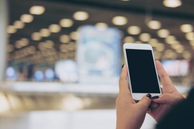 Bir kadın tutarak ve süre ayakta ve Bagaj talep havaalanında bekleyen boş siyah perde ile beyaz cep telefonu kullanarak mockup görüntü