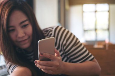 Gülen yüz ve duygu ile akıllı telefon kullanan güzel Asyalı kız modern kafede sakin ol