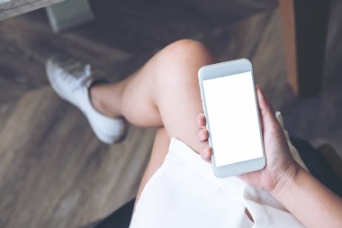 Modern ahşap zemin arka plan ile uylukta boş ekran ile beyaz cep telefonu tutan kadının el mockup görüntü