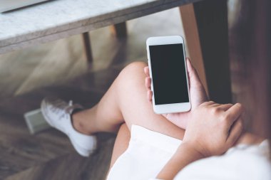 Modern ahşap zemin arka plan ile uylukta boş ekran ile beyaz cep telefonu tutan kadının el mockup görüntü